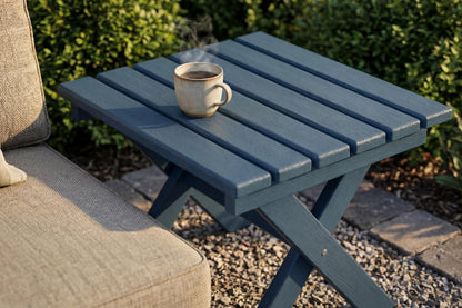 Blue outdoor side table with a cup on it, next to a chair with a cushion.