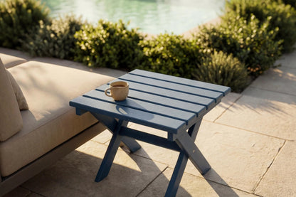 Blue outdoor table with a cup on it, next to a beige sofa by a pool.