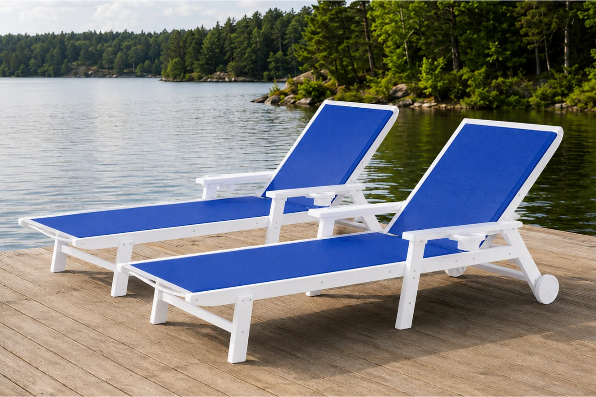 Two blue and white outdoor chaise lounge chairs positioned on a wooden deck next to a calm lake with a forest shoreline in the background.