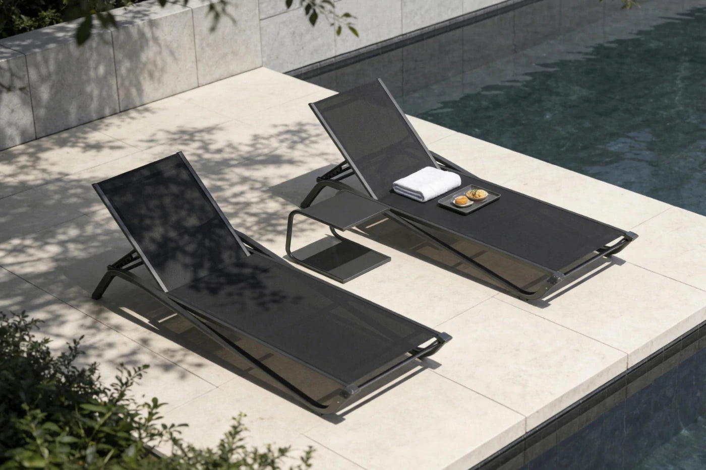 Two black lounge chairs by a poolside with a towel and small tray.
