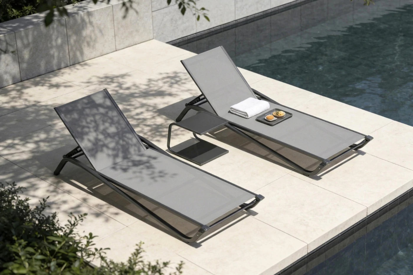 Two gray lounge chairs by a poolside with a towel and small items on one of them.