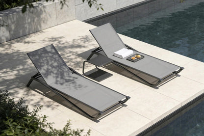 Two gray lounge chairs by a poolside with a towel and small items on one of them.