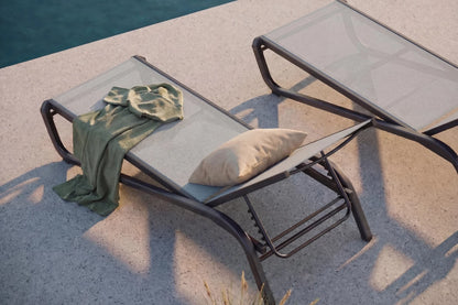 Two lounge chairs by a poolside with a towel and pillow on one of them.