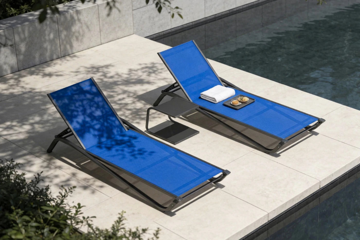 Two blue lounge chairs by a poolside with a towel and a plate on one of them.