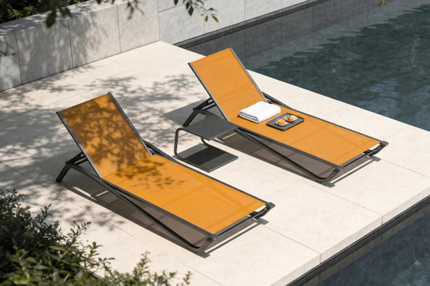 Two orange lounge chairs by a poolside with a towel and small table.