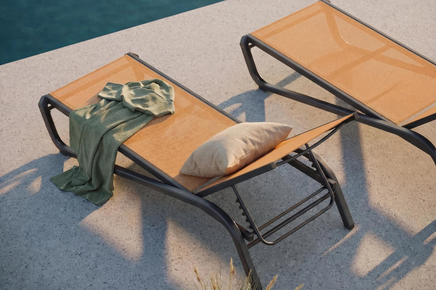 Two lounge chairs by a poolside with a towel and pillow on one of them.