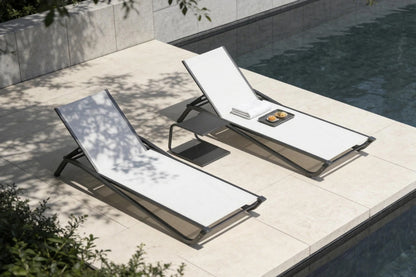 Two white lounge chairs on a patio next to a pool.