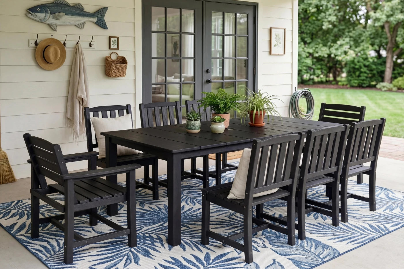 Outdoor dining set with black table and chairs on a patio, featuring a rug and plants.