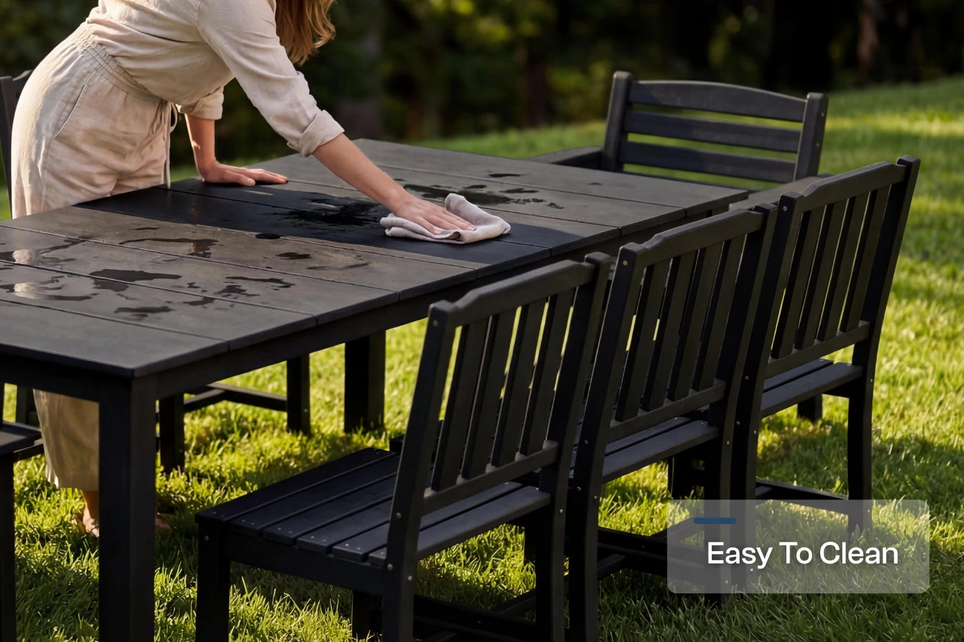 Person cleaning a outdoor table with chairs on a grassy area, emphasizing ease of cleaning.