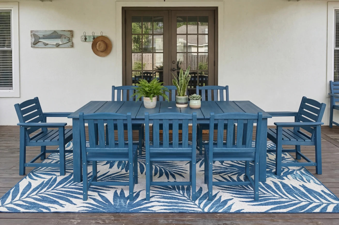 Blue outdoor dining set on a wooden deck with a white wall and door in the background.