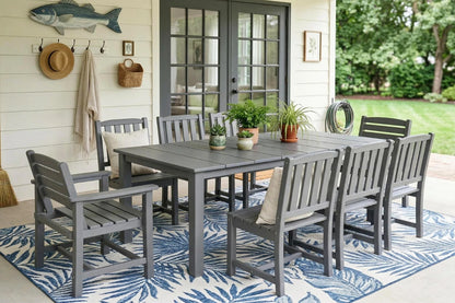 Outdoor dining set with gray furniture on a patio with a rug and plants.