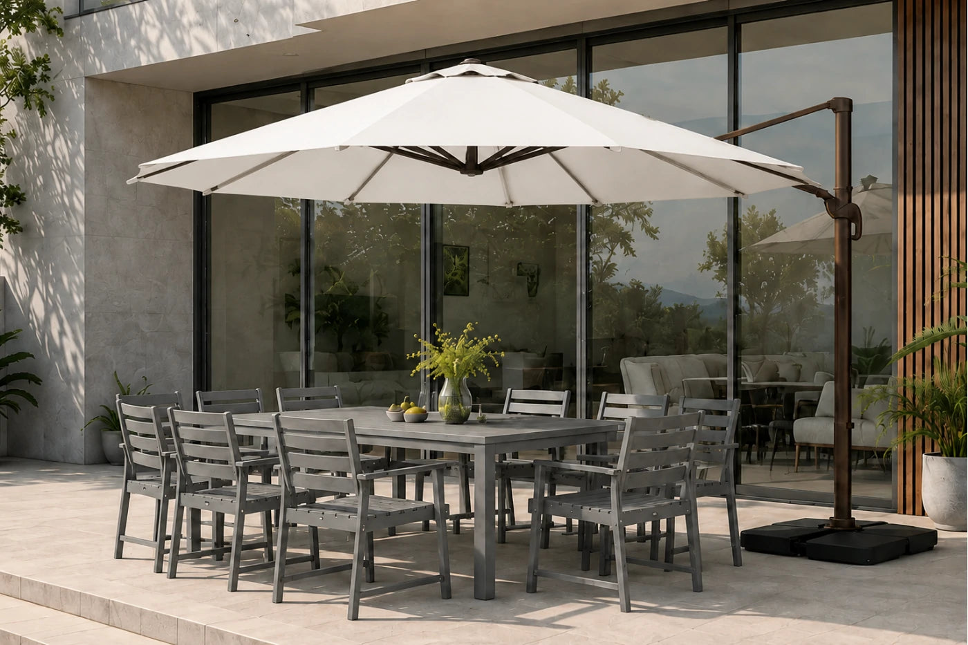 Outdoor patio dining set with a rectangular gray slat table, eight matching gray chairs, a large creamy white cantilever umbrella, and a black base, staged in front of a modern glass-walled building.