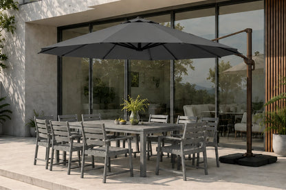 A large dark gray patio umbrella with a dark metal cantilever pole and base stands beside a gray outdoor dining table and chairs on a modern patio in front of large glass windows.