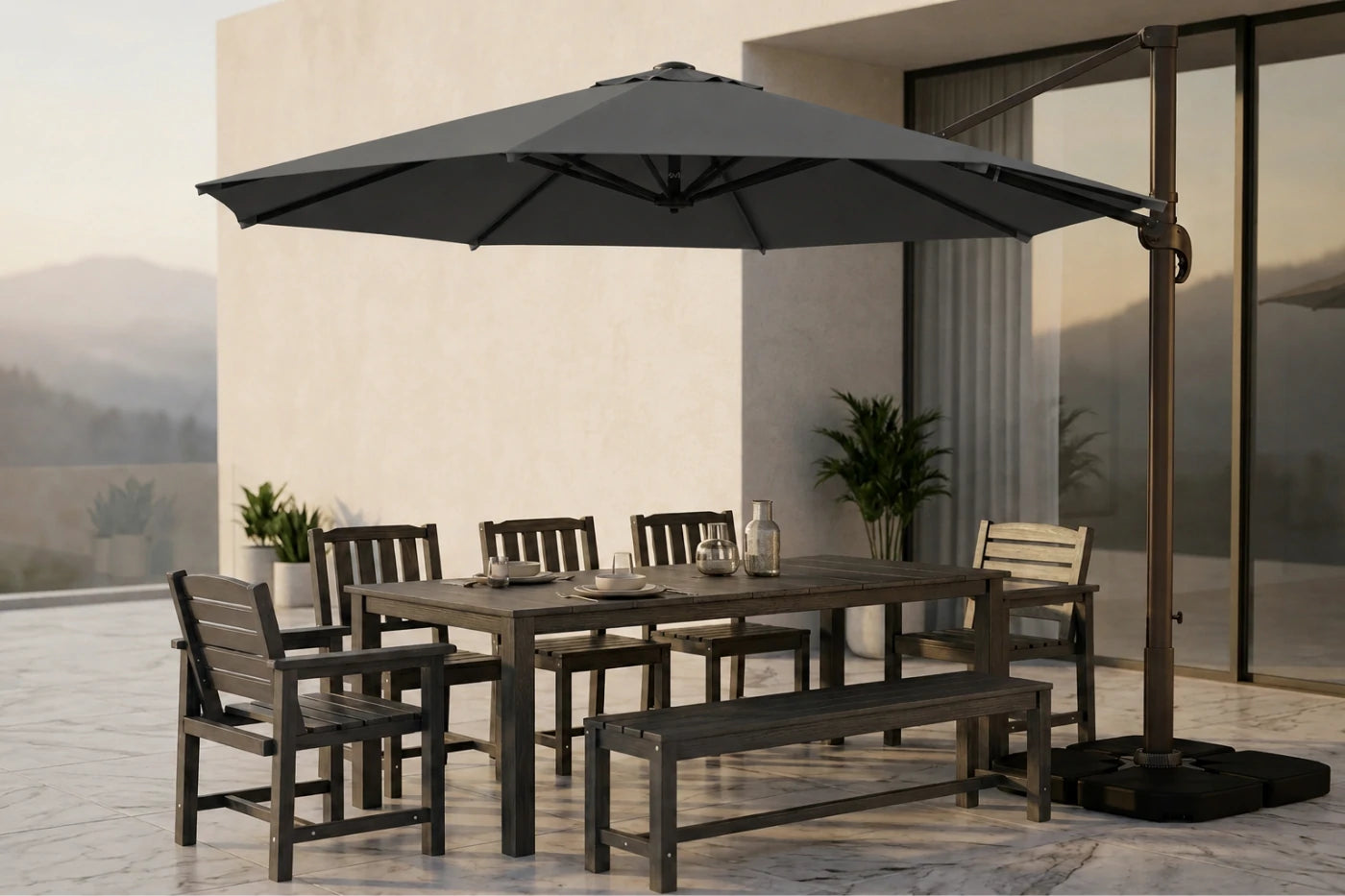 A large dark gray cantilever patio umbrella with a dark metal frame and base, shading a rectangular dining table, four chairs, and a bench on a modern outdoor patio.
