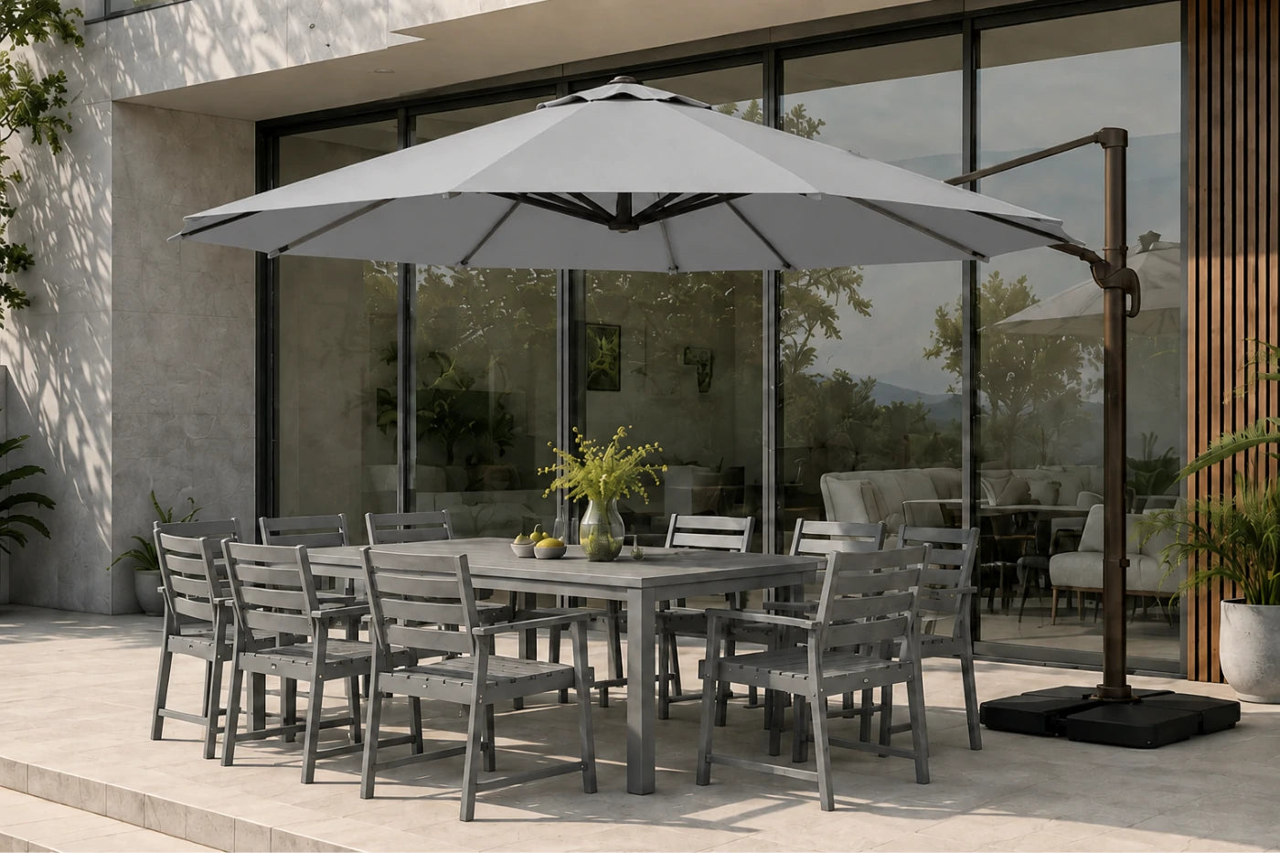 Gray outdoor patio dining set with a rectangular table and matching chairs, shown under a large gray cantilever patio umbrella on a paved terrace in front of a modern glass building.