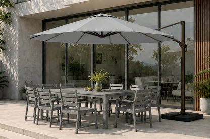 Gray outdoor patio dining set with a rectangular table and matching chairs, shown under a large gray cantilever patio umbrella on a paved terrace in front of a modern glass building.