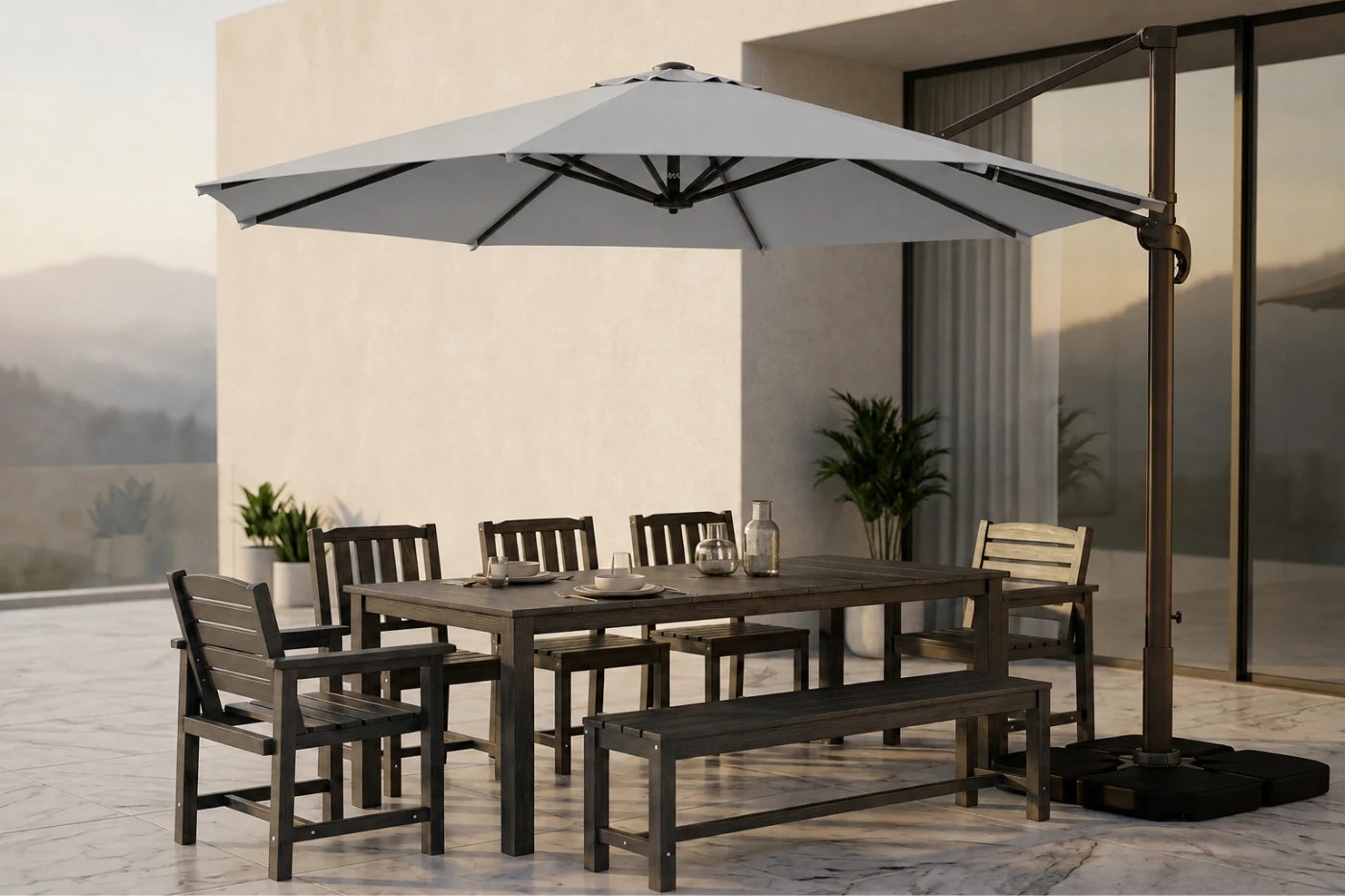 A large gray cantilever patio umbrella with a dark metal frame and base, shading a rectangular dining table, four chairs, and a bench on a modern outdoor patio.