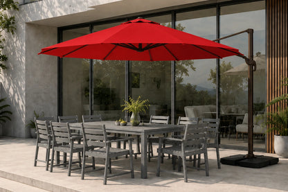 A large red patio umbrella with a dark metal cantilever pole and base stands beside a gray outdoor dining table and chairs on a modern patio in front of large glass windows.