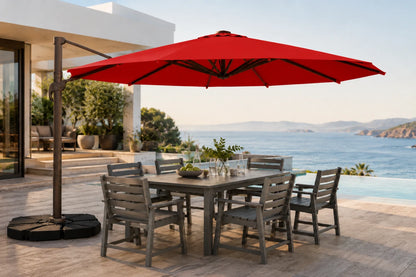 A large red cantilever patio umbrella with a square base is shown outdoors on a stone terrace beside a dining table and chairs, with a pool and ocean view in the background.
