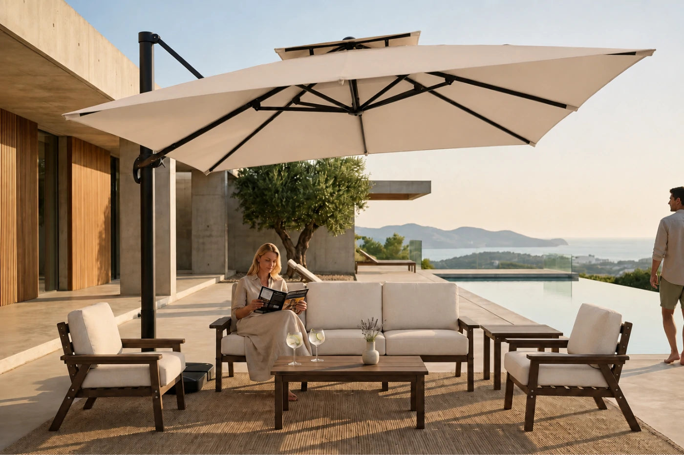 Outdoor patio furniture set with a large beige cantilever umbrella, a beige sofa, two matching armchairs, and a low wooden coffee table, shown in a luxurious modern villa setting with a pool and a woman sitting on the sofa.