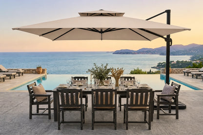 Outdoor patio dining set with a rectangular dark wood table, matching slatted chairs, a large beige patio umbrella, and a pool overlooking the sea at sunset.
