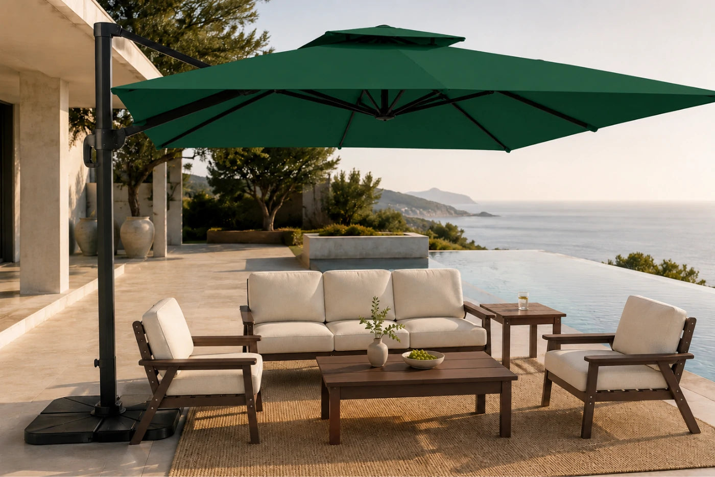 A large dark green cantilever patio umbrella shading a modern outdoor furniture set with a sofa, two armchairs, a coffee table, and a side table on a poolside terrace.