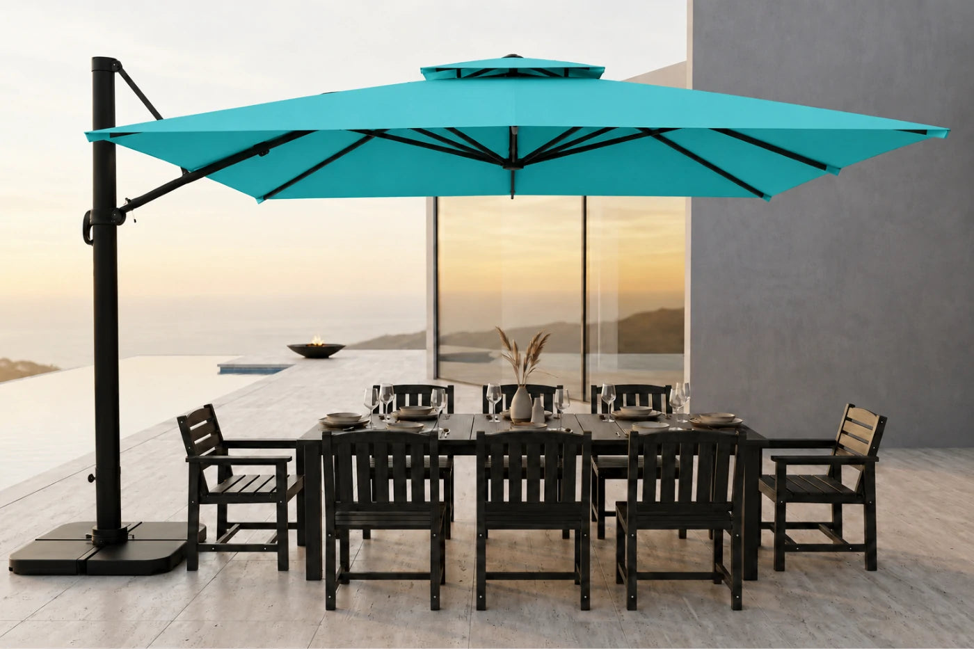 A large turquoise cantilever patio umbrella with a black pole stands beside a dark outdoor dining table and chairs on a patio at sunset.