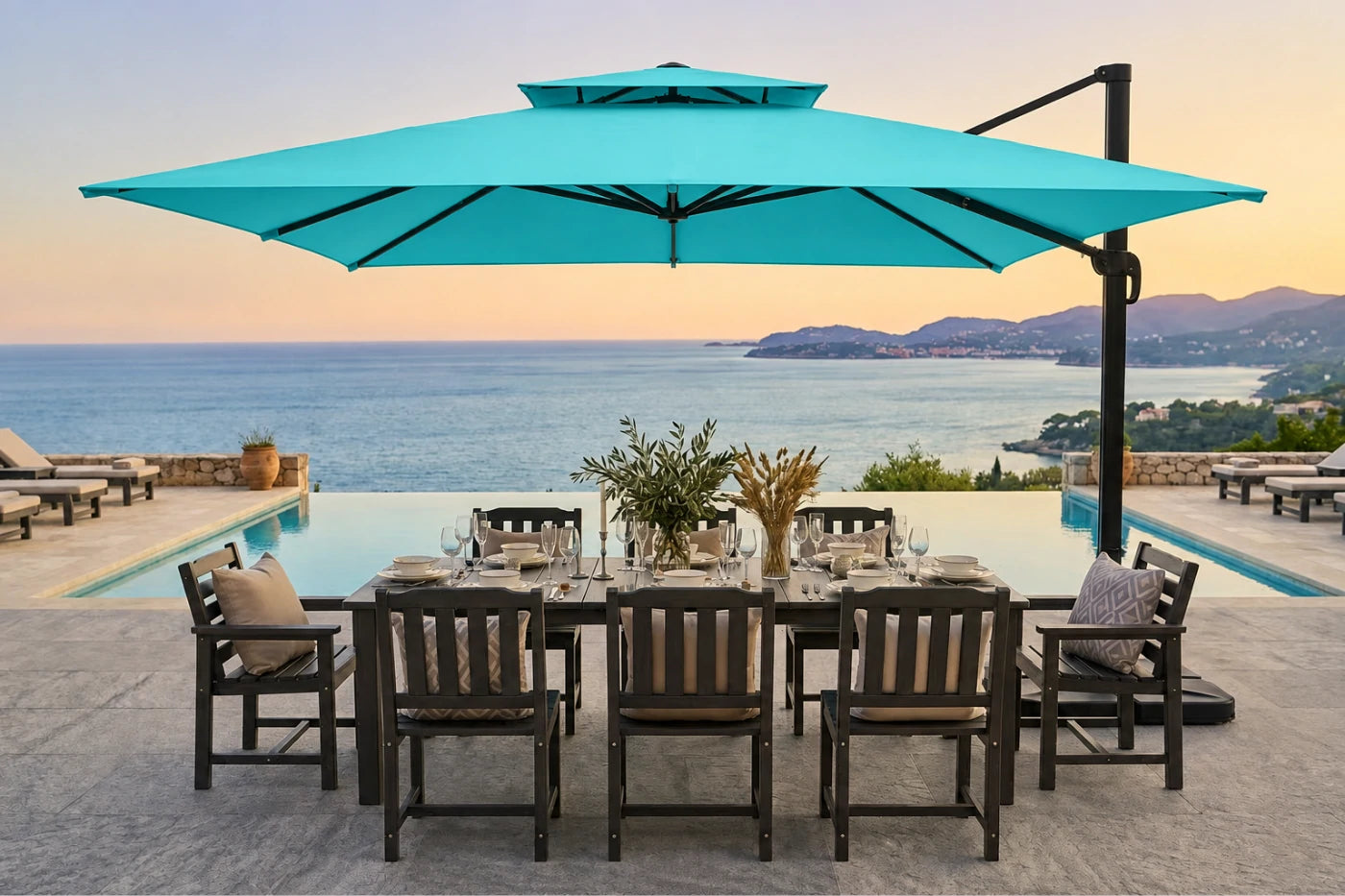 A large turquoise cantilever patio umbrella over a dining table and chairs next to an infinity pool with an ocean sunset view in the background.
