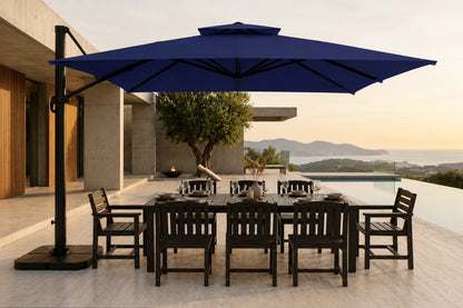 A large navy blue cantilever patio umbrella with a black metal frame and base, shading a dark outdoor dining table and chairs on a modern terrace overlooking a pool and distant mountains.