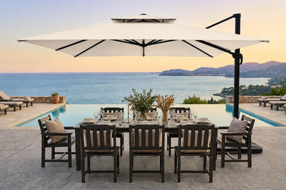 Outdoor dining set with a rectangular dark wood table, six matching chairs, and a large white patio umbrella overlooking an infinity pool and ocean view at sunset.