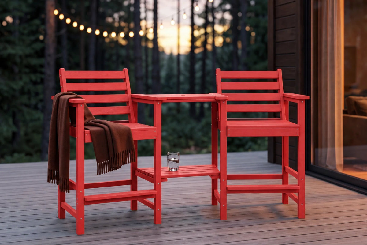 A red three-piece outdoor patio bar set consisting of two high-back armchairs and a small square side table, shown on a wooden deck at dusk with a brown throw blanket draped over one chair.