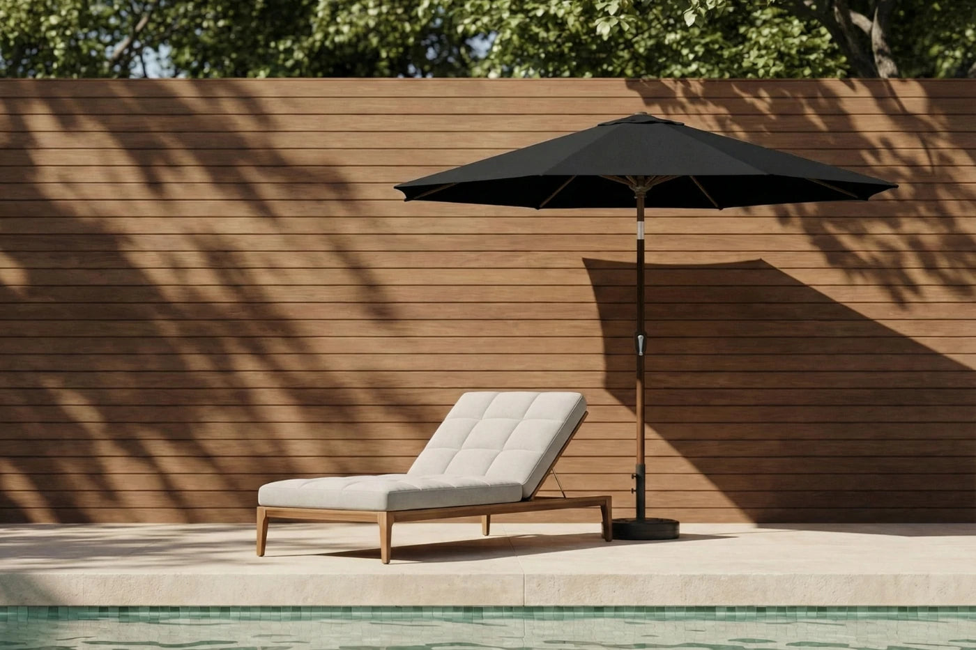 Chaise lounge with a black umbrella by a poolside against a wooden wall.