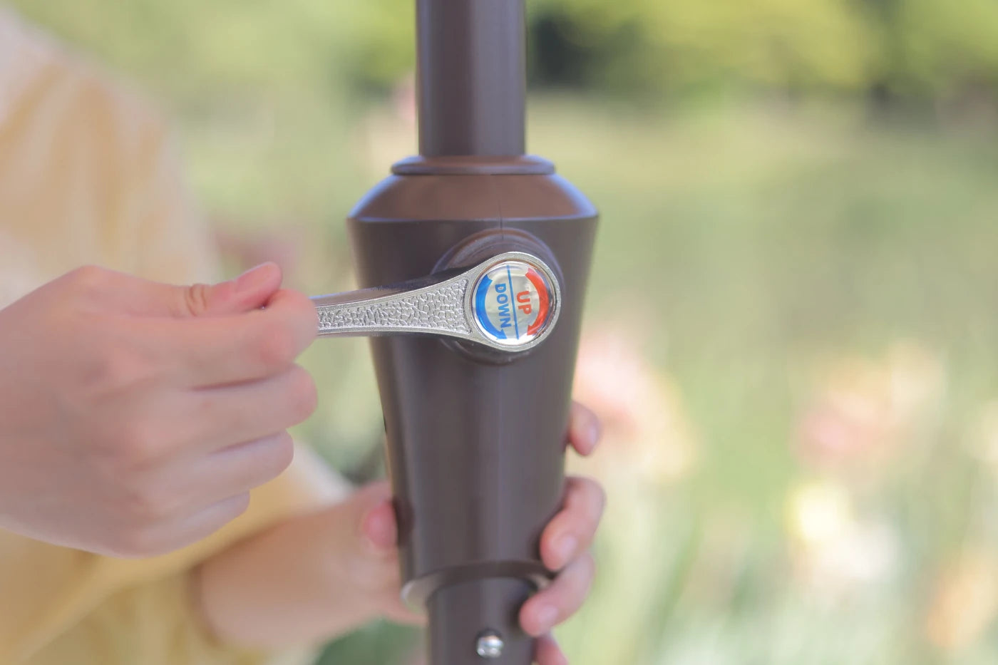Person holding a brown outdoor umbrella with a visible brand logo against a blurred natural background