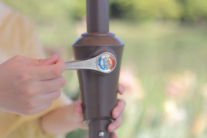 Person holding a brown outdoor umbrella with a visible brand logo against a blurred natural background