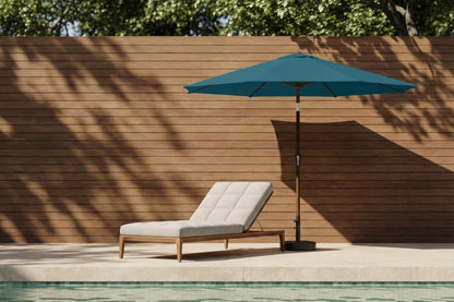 Chaise lounge with a teal umbrella by a poolside against a wooden wall.
