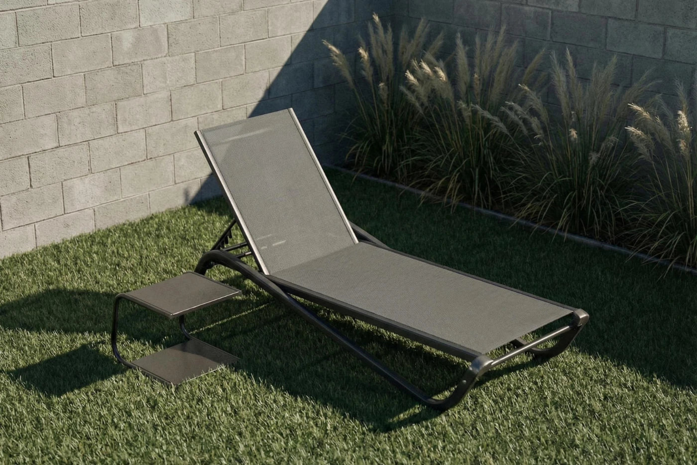 Gray lounge chair on grass with a stone wall and plants in the background