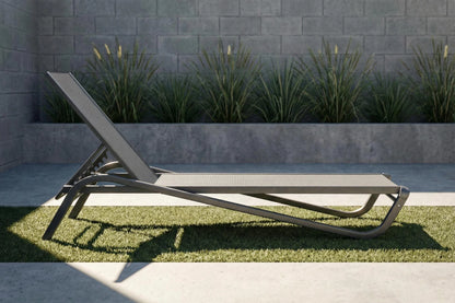 Modern outdoor lounge chair on grass with a stone wall and plants in the background