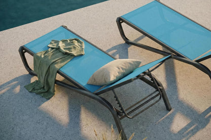 Two blue lounge chairs with a green towel and pillow by a poolside.