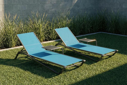 Two blue lounge chairs on grass with a stone wall background