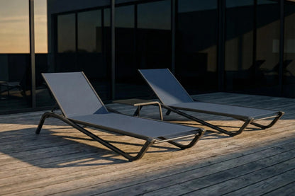 Two lounge chairs on a wooden deck with a dark building in the background.