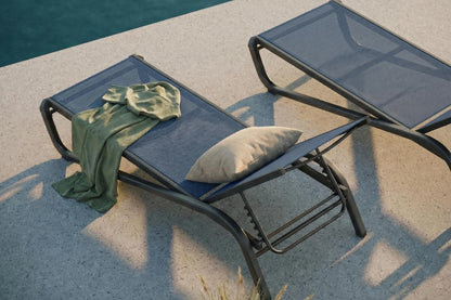 Two lounge chairs by a poolside with a towel and pillow on one of them.