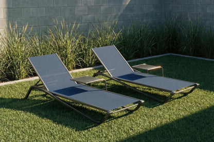 Two lounge chairs on grass with a stone wall and plants in the background