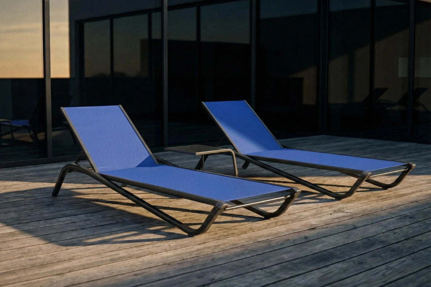 Two blue lounge chairs on a wooden deck with a dark building in the background.