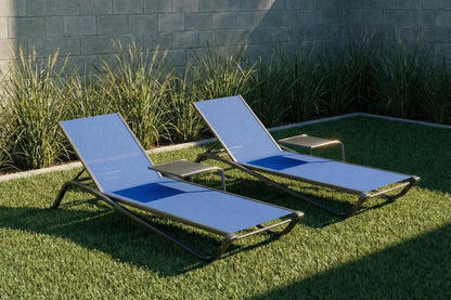 Two blue lounge chairs on grass with a stone wall and plants in the background