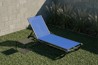 Blue lounge chair on grass with a stone wall and plants in the background