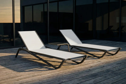 Two white lounge chairs on a wooden deck with a dark building in the background.