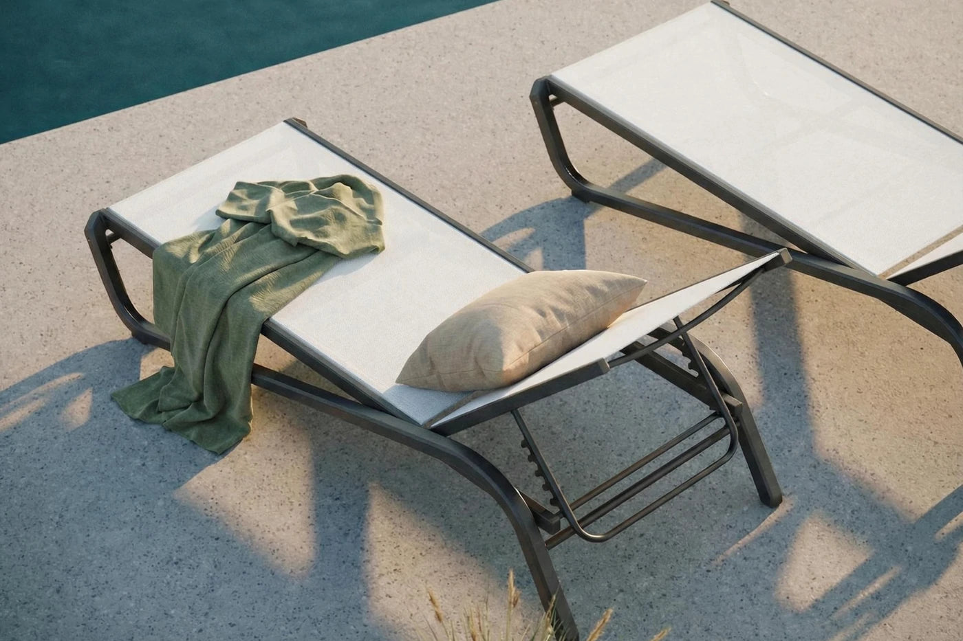 Two lounge chairs by a poolside with a towel and pillow on one of them.