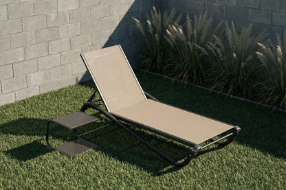Beige lounge chair on grass with a stone wall and plants in the background
