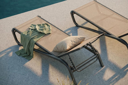 Two lounge chairs by a poolside with a green towel and beige pillow.