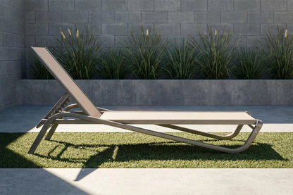 Modern outdoor lounge chair on grass with a stone wall and plants in the background